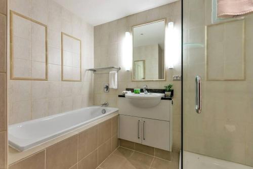 a bathroom with a tub and a sink and a mirror at Sun Soaked Corner Apartment with Harbour View in Auckland