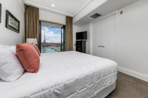 a bedroom with a large white bed with a window at Sun Soaked Corner Apartment with Harbour View in Auckland