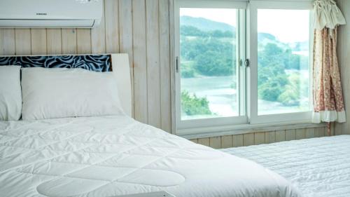 a bedroom with a white bed and a window at Yeosu Sky Pension in Yeosu