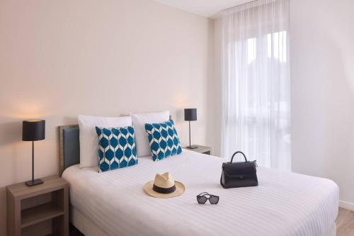 a white bed with a hat and sunglasses on it at Quality Aparthotel Morangis Orly in Morangis