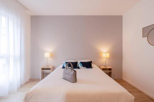 a white bedroom with a bed with a purse on it at Quality Aparthotel Bourgoin-Jallieu in Bourgoin