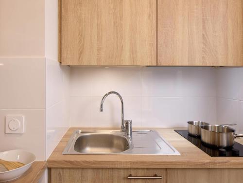 a kitchen with a stainless steel sink and wooden cabinets at Quality Aparthotel Plerin Saint Brieuc in Plérin