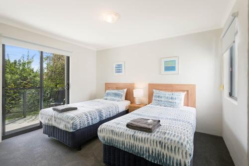 two beds in a room with a window at Seachange Apartments Merimbula in Merimbula