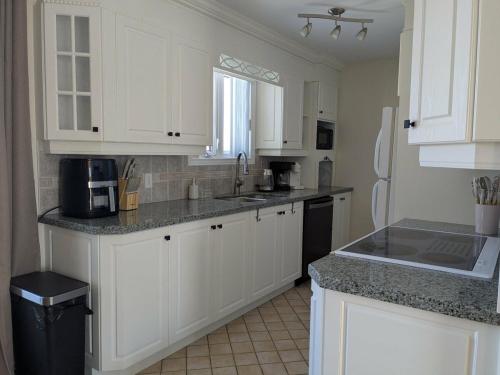 a kitchen with white cabinets and a black refrigerator at Chez nous ailleurs in Sainte-Anne-des-Monts