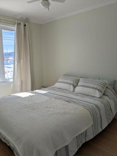 a bed in a white bedroom with a window at Chez nous ailleurs in Sainte-Anne-des-Monts