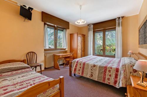 a bedroom with two beds and a desk and windows at Hotel Valentino - Bionaz in Bionaz