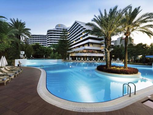 ein großer Swimmingpool mit Palmen vor einem Gebäude in der Unterkunft Rixos Downtown Antalya - The Land Of Legends Access in Antalya