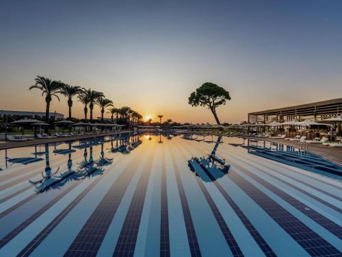 an empty swimming pool with palm trees and the sunset at Rixos Premium Belek - The Land of Legends Access in Belek