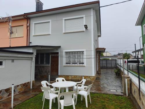 a patio with white chairs and a table in front of a house at A Pedriña Ribadeo in Ribadeo