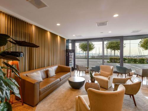 a living room with couches and chairs and windows at Mövenpick Hotel Lausanne in Lausanne