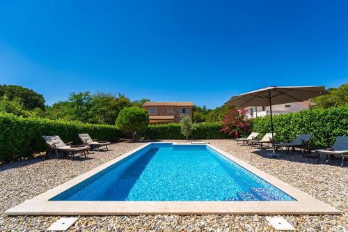 a swimming pool with chairs and an umbrella at Villa Pepina in Risika