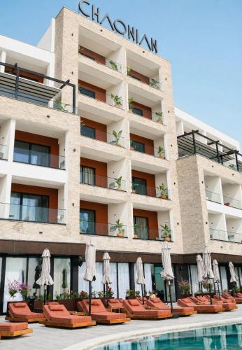 a hotel with chairs and umbrellas next to a swimming pool at Chaonian Hotel in Dhërmi