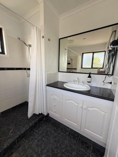 a white bathroom with a sink and a mirror at Beachside Studio Apartment in Bargara
