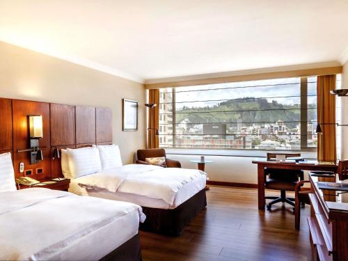 a hotel room with two beds and a desk and a window at Swissotel Quito in Quito
