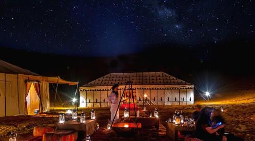 a woman standing in front of a building at night at Camel Trekking Camp & Activities in Merzouga