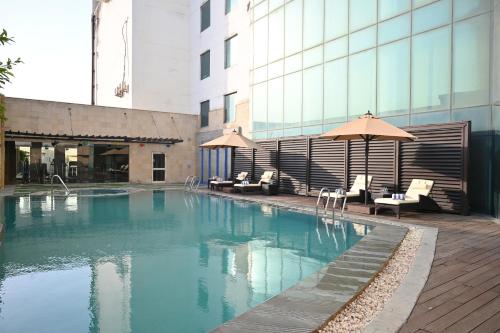 a swimming pool with chairs and umbrellas next to a building at Savoy Suites Greater Noida in Greater Noida