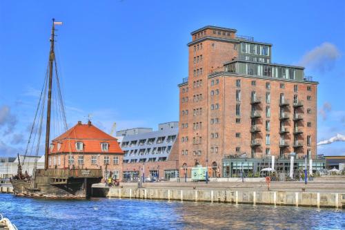 a tall brick building next to a river with a boat at Ohlerich Speicher App_ 04 in Wismar