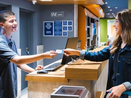 a woman handing a man a credit card at a cash register at ibis budget Pindamonhangaba in Pindamonhangaba