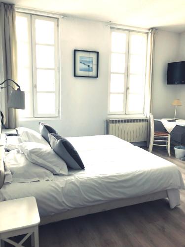 a bedroom with a large white bed with two windows at Hôtel Le Galet Bleu in Fouras