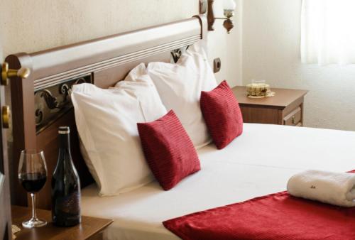 a bed with red and white pillows and a glass of wine at Family Hotel Dinchova kushta in Rozhen