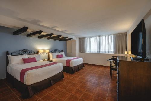 a hotel room with two beds and a flat screen tv at Gamma Merida El Castellano in Mérida
