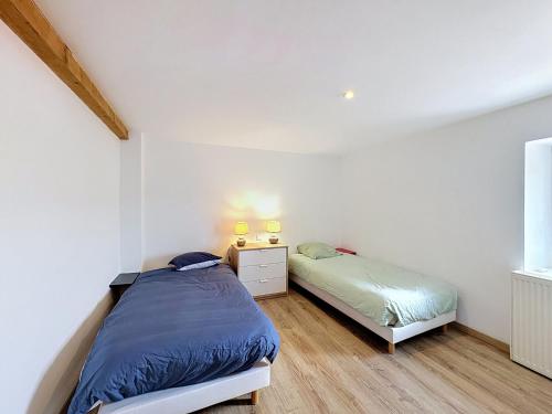 two beds in a bedroom with white walls and wood floors at La Grande Chaumiere in Saint-Vulbas
