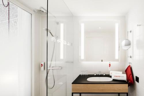 a white bathroom with a sink and a shower at IntercityHotel Braunschweig in Braunschweig