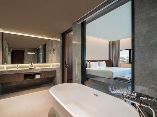 a bathroom with a tub and a bedroom with a bed at Novotel Pontianak Convention Centre in Pontianak