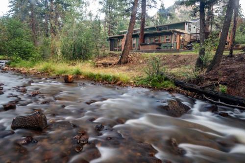 a house in the woods with a stream in front of it at Stonebrook Resort - Adult Only in Estes Park
