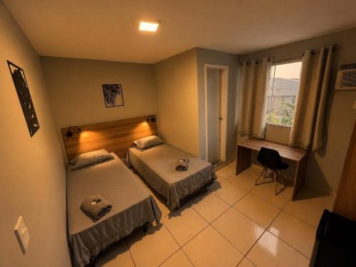 a bedroom with two beds and a desk and a window at DLUX Hotel in Campos dos Goytacazes