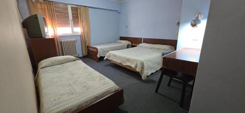 a room with two beds and a desk and a television at Hotel Oviedo in Río Gallegos