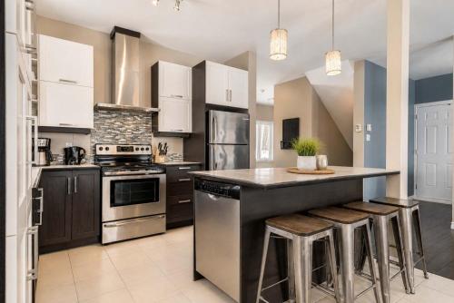 a kitchen with stainless steel appliances and a counter with stools at Le Haut-Perche - Spa and River View in Petite-Rivière-Saint-François