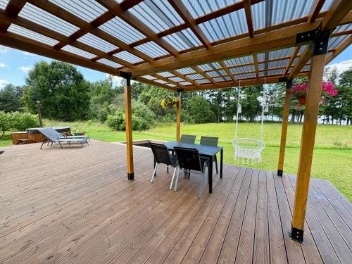 a wooden deck with a table and chairs under a pergola at Rātes Krasti - Rasa - holiday house with sauna and lakeview in Lejasciems
