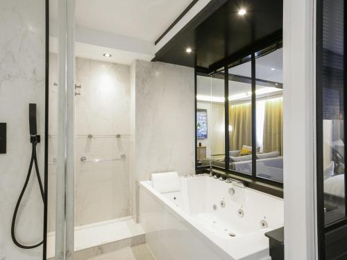 a bathroom with a tub and a shower and a bedroom at Mercure Bordeaux Aéroport in Mérignac