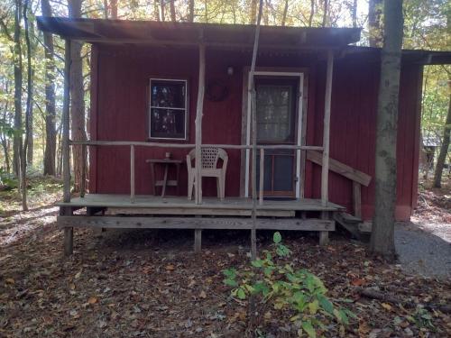 a red cabin in the woods with a chair on the porch at Thunder Ridge Cabins B&B - Bird Nest in Rockbridge