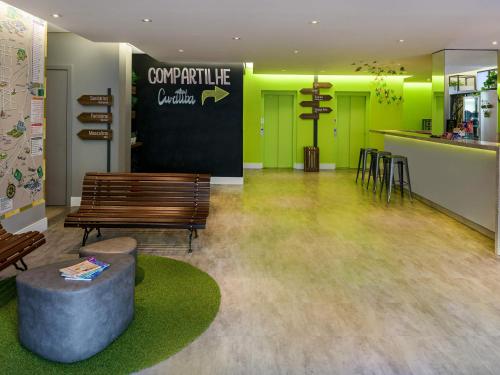 a lobby with a bench and a bar with green doors at ibis Styles Curitiba Centro Civico in Curitiba