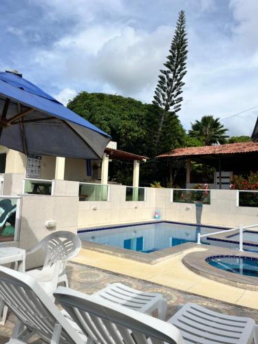a pool with chairs and an umbrella next to a building at Villa Velha Flats in Itamaracá