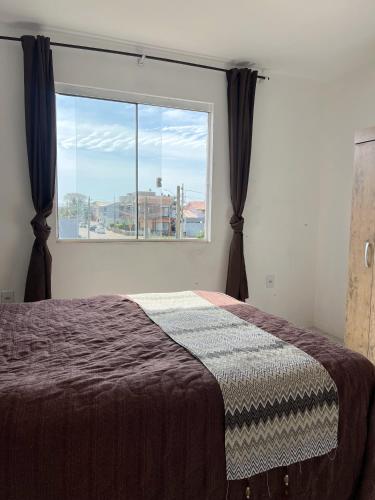 a bedroom with a bed and a large window at Apartamento em Garopaba in Garopaba
