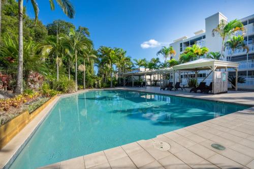a swimming pool with palm trees and a building at Moreton Island Villas and Apartments in Tangalooma