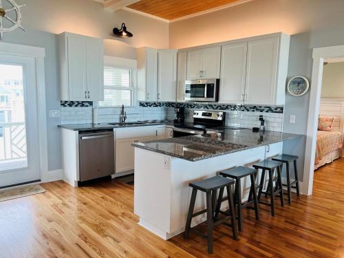 a kitchen with white cabinets and a island with bar stools at Holden R Breath in Holden Beach