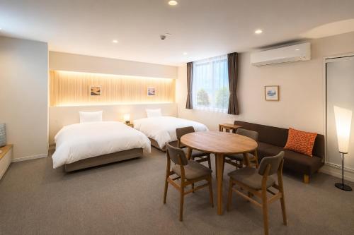 a hotel room with two beds and a table and a couch at NAGI Hiroshima Hotel and Lounge in Hiroshima