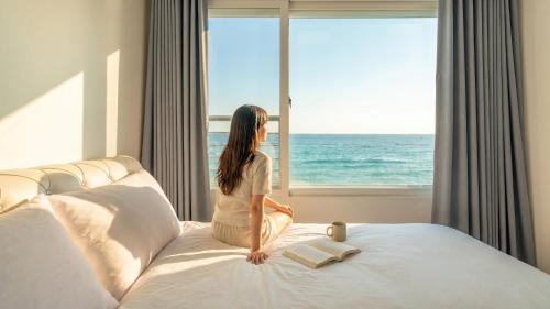 a woman sitting on a bed looking out at the ocean at GoSeong Beach Jin Spa Pension in Goseong