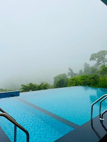 a large blue swimming pool with trees in the background at Hill Breeze Pool Resort Vagamon by VOYE HOMES in Vagamon