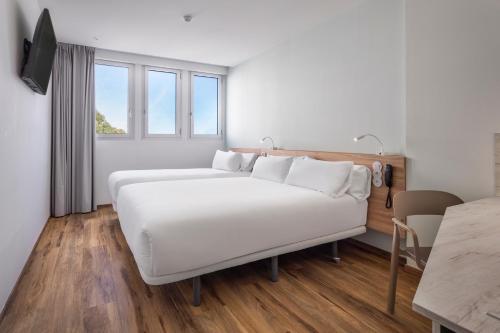 a bedroom with a large white bed and a table at B&B HOTEL Lisboa Aeroporto in Lisbon