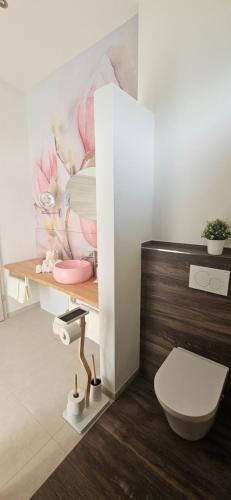 a bathroom with a toilet and a flower painting on the wall at Gartenbungalow Rhönwild in Hilders
