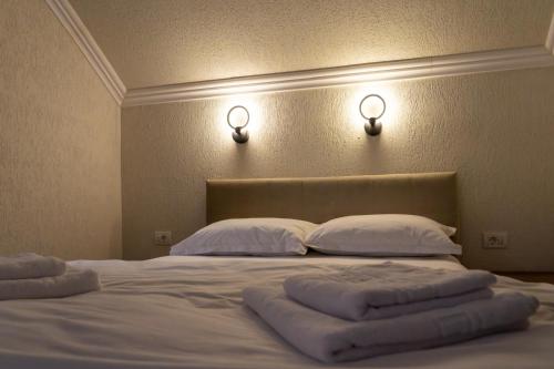 a bed with white pillows and two lights on the wall at Vila dintre Brazi in Râu de Mori