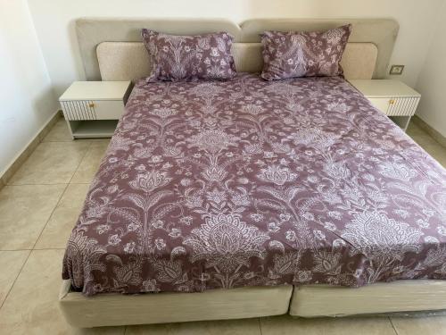 a bed with a purple comforter and two tables at Apparemment La Perla in Banzart