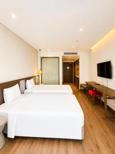 two beds in a hotel room with a desk and a television at Thanh Son Apartment Mui Ne Beachfront in Ấp Thiẹn Ái