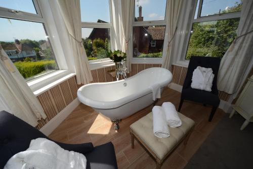 a bathroom with a tub and a chair and windows at Seabrook House Hotel in Hythe