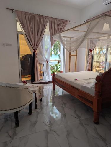 a bedroom with a canopy bed and a chair at Nisandra Beach Hotel in Nungwi